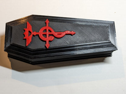 Close up of a black 3D printed coffin shaped dice/trinket box with a red alchemy symbol decoration