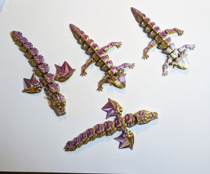 Four 3D printed articulated creatures in purple bronze. 2 are dragons with wings and 2 are adorable lizards