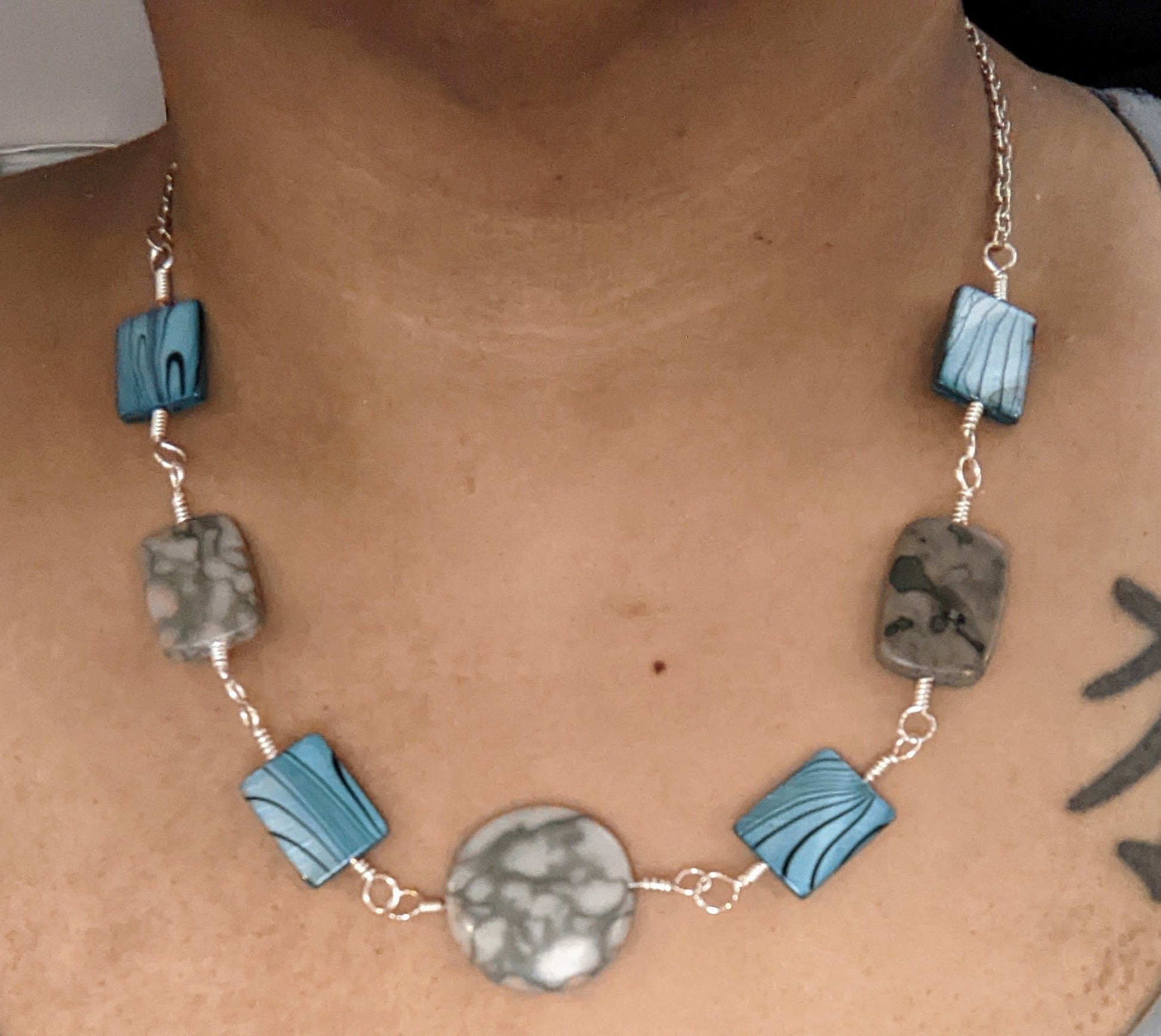 Close up of a neck wearing a linked component necklace.  The wire wrapped links are of grey marble canyon and dyed shell alternating.  The center is a round marble canyon bead and the other beads are rectangular. 