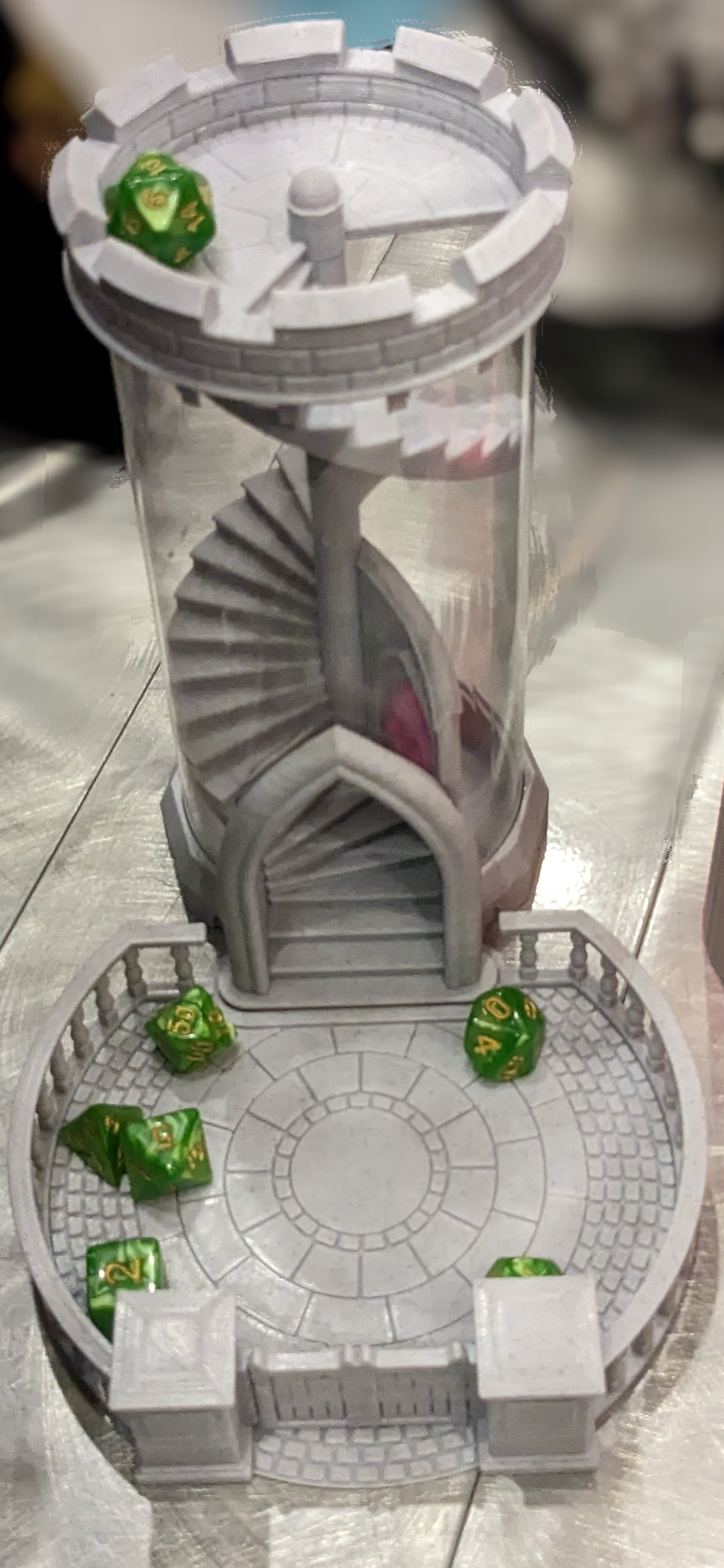 3D printed dice tower and tray in the shape of a castle tower and courtyard.  A set of green and yellow dice sit in the tray with the D20 on top of the tower waiting to roll.