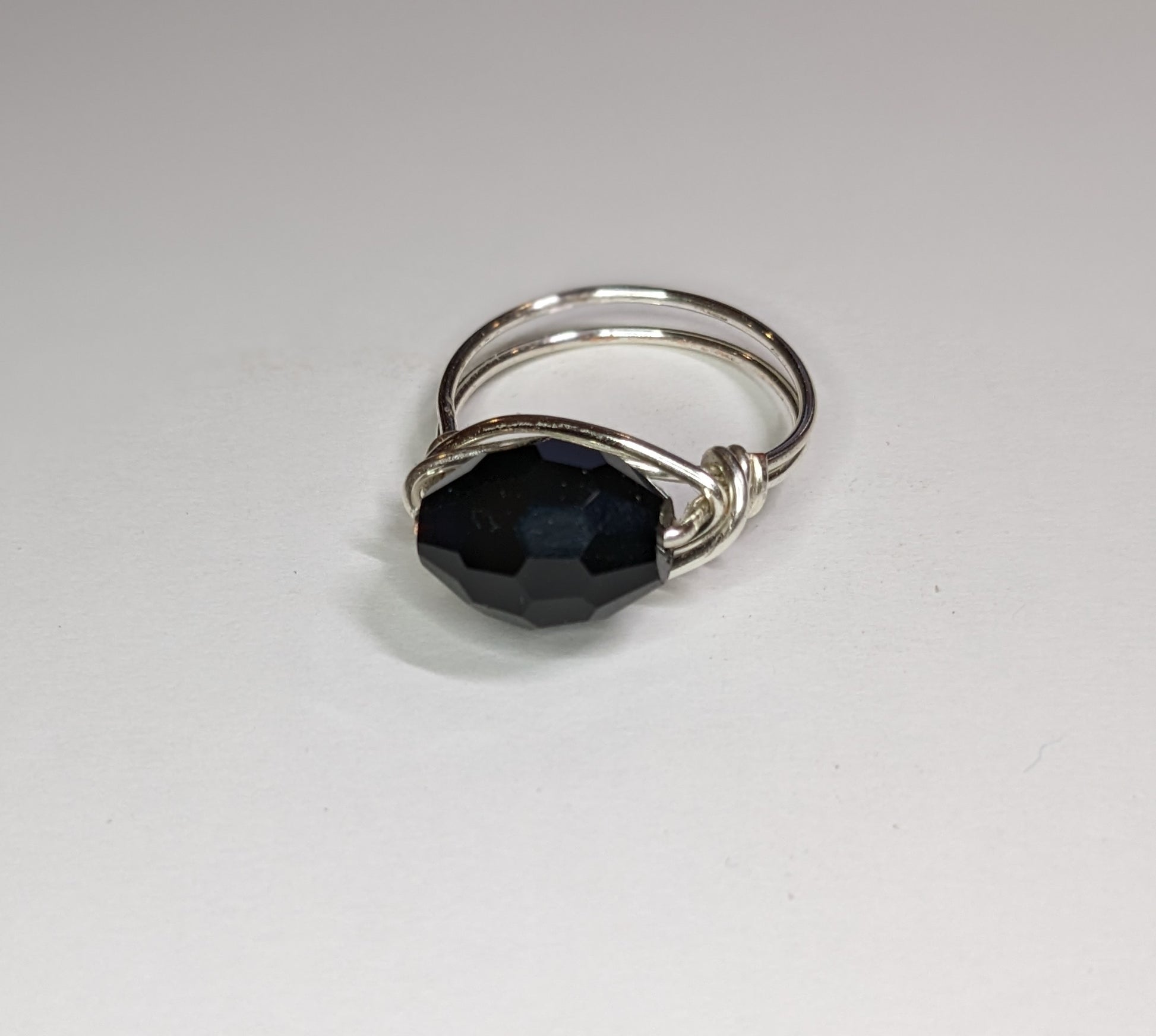 Close up for wire wrapped black glass faceted ring with ring pointing slightly to the left to show details.