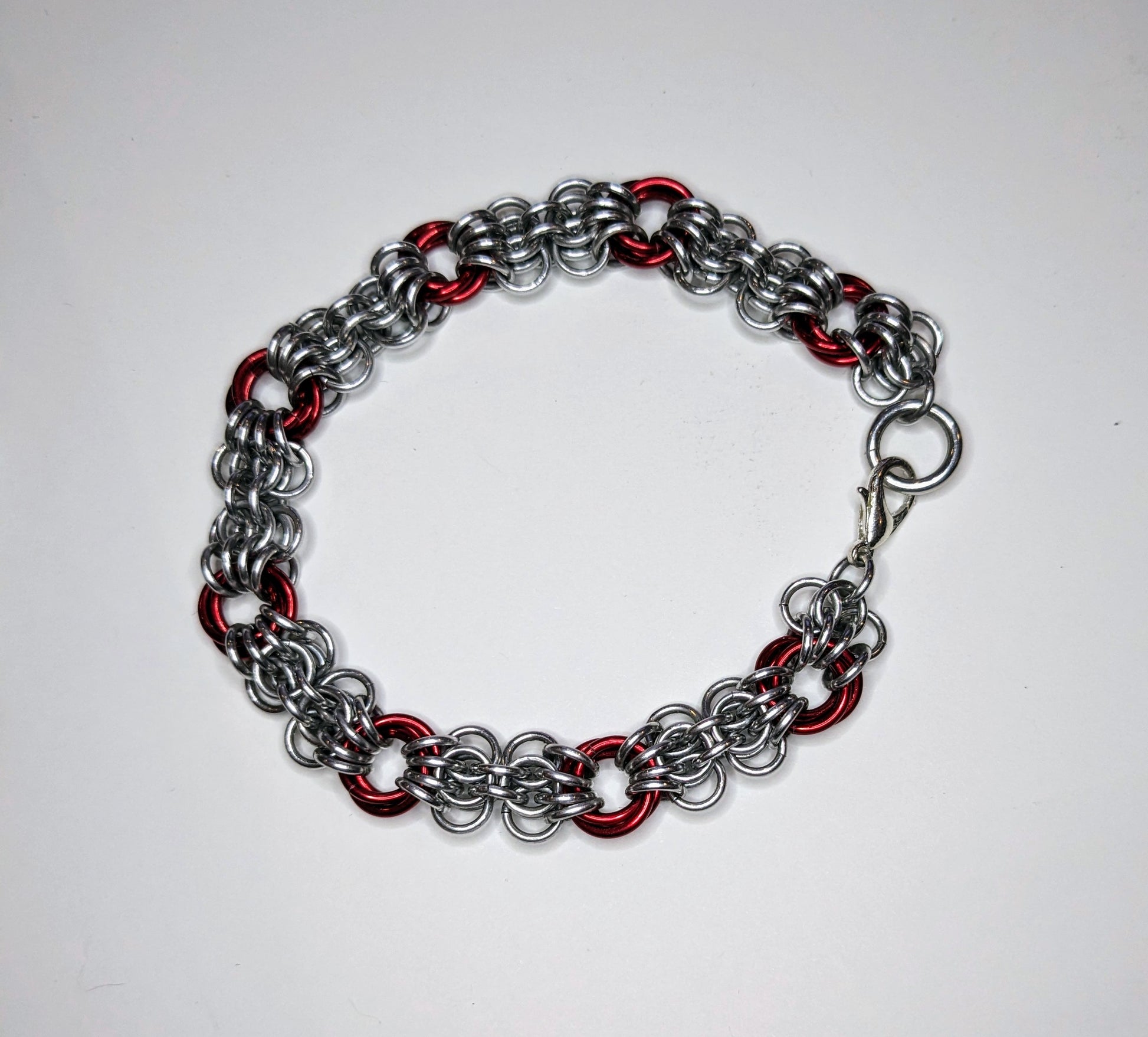 Silver and red butterfly weave chainmail bracelet on a white background.  Bracelet has a lobster clasp.