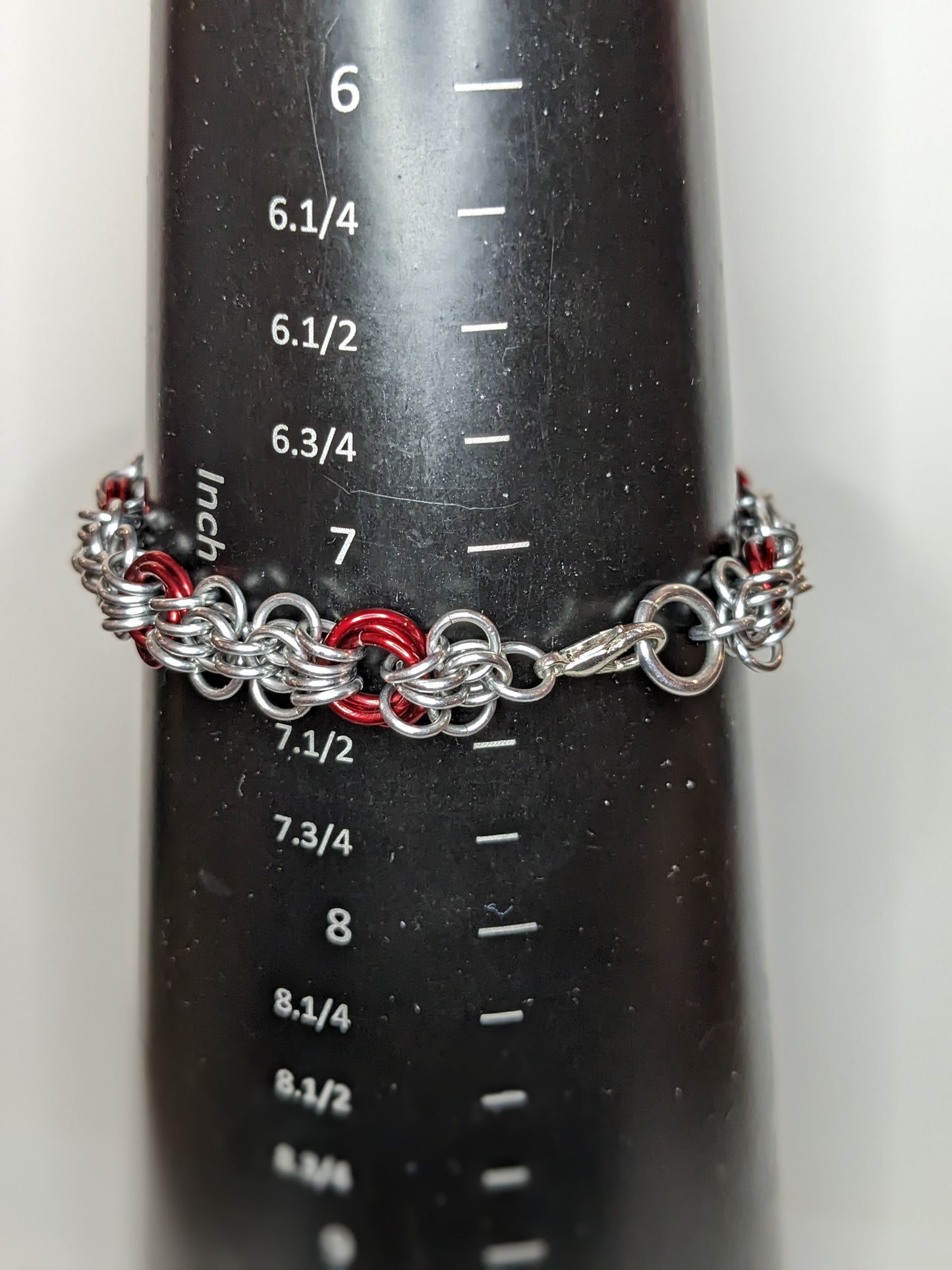 Silver and red butterfly weave chainmail bracelet on a black bracelet mandrel showing the braceleet is 7.25 inches