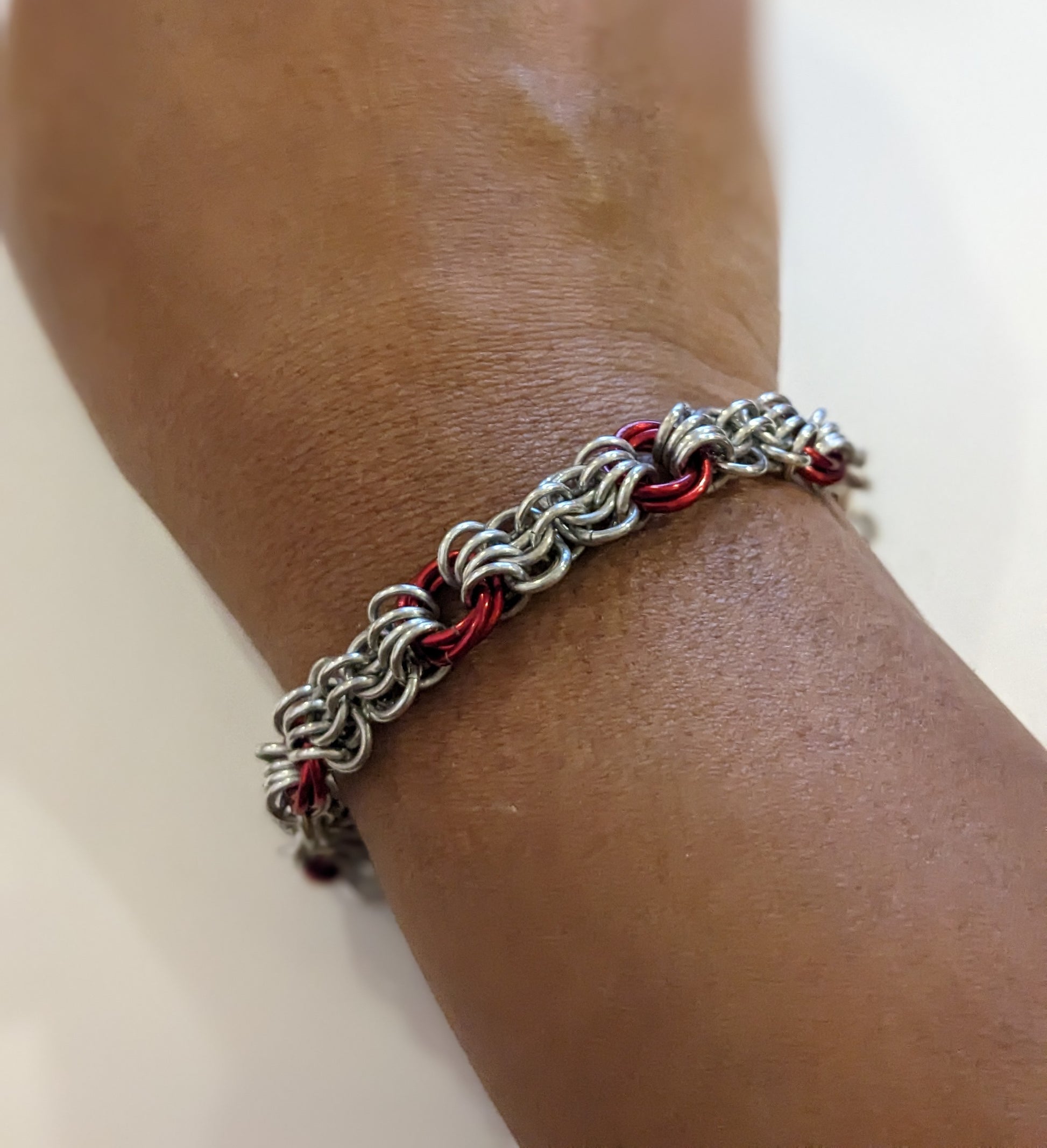 Silver and red butterfly weave chainmail bracelet on a brown wrist