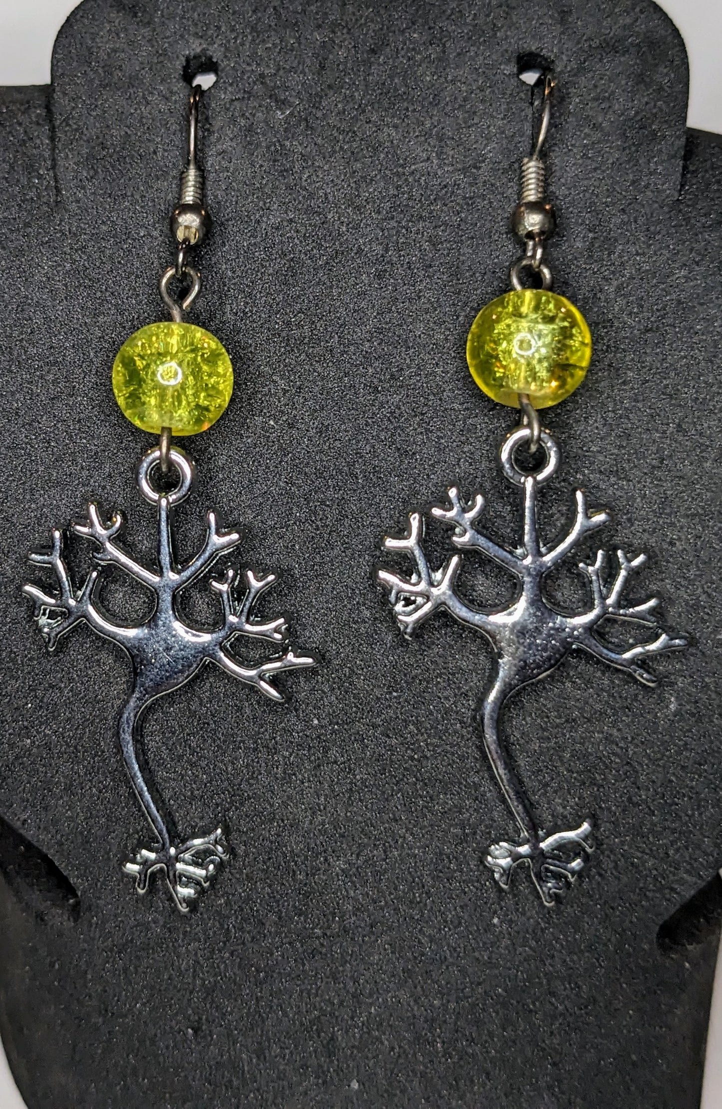 Earrings on a black display.  Earrings are silver neuron charms with a yellow glass crackle bead