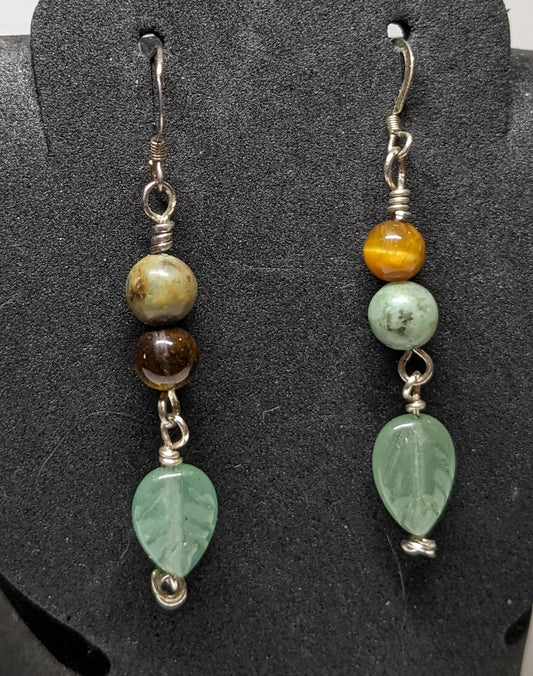 Close up of earrings. Earrings have African turquoise and tiger eye beads and a peridot leaf charm. They are asymmetrical with the gemstones reversed on one.