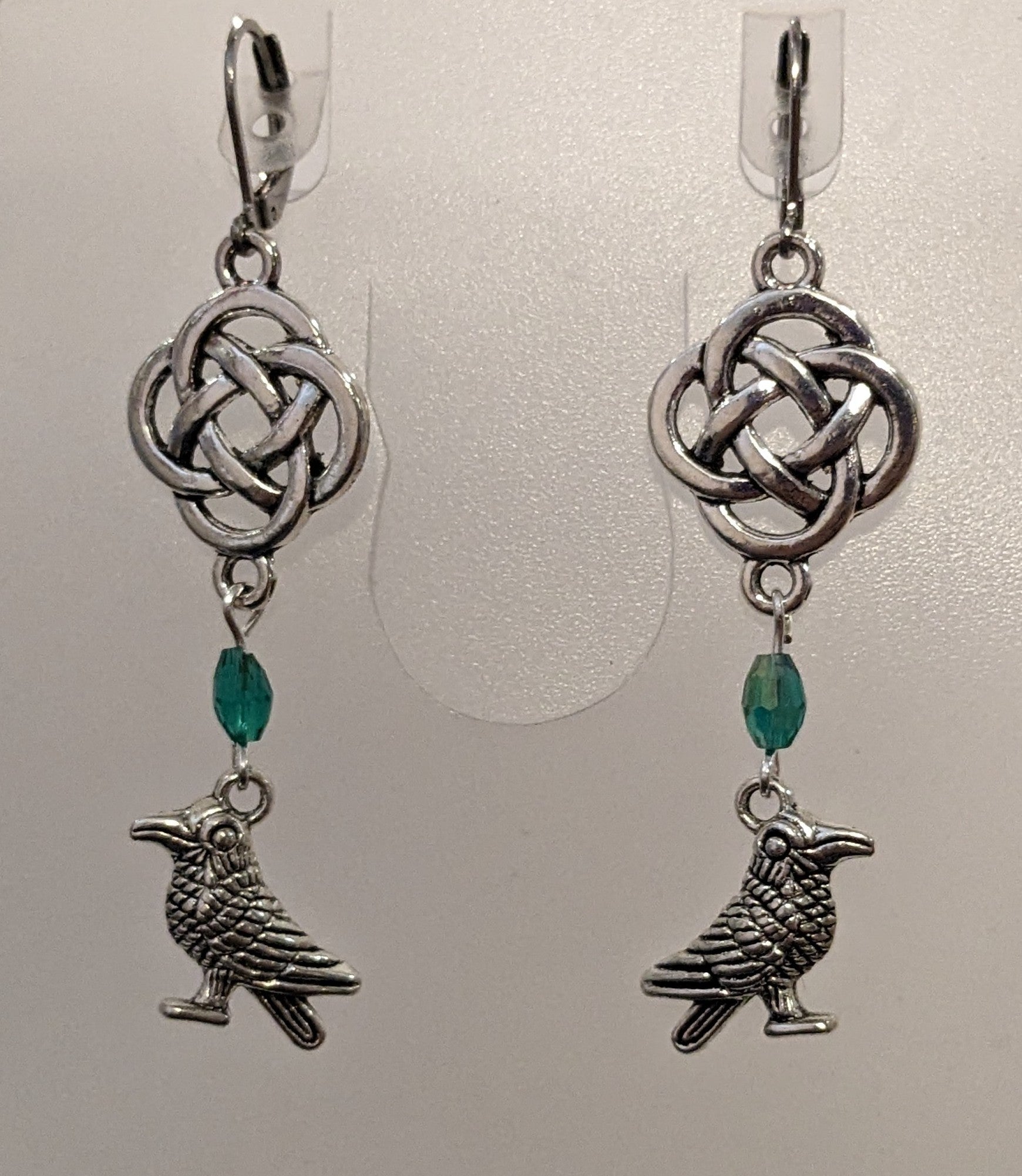 Earrings with silver toned raven charms, a blue - green crystal beads and a silver Celtic knot. 