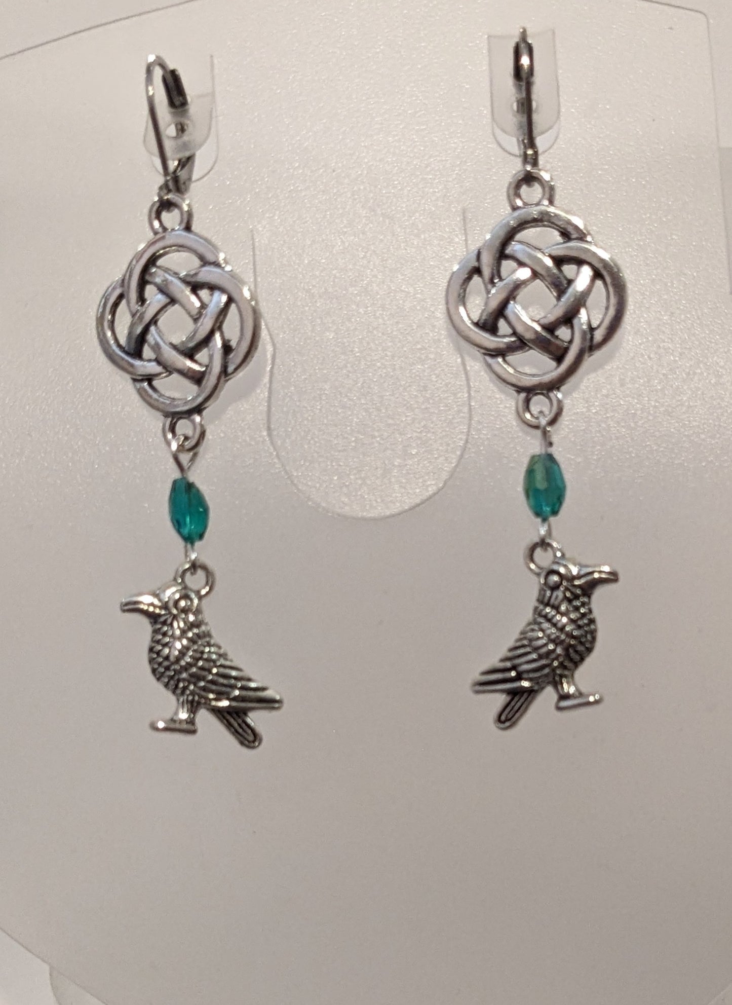 Earrings with silver toned raven charms, a blue - green crystal beads and a silver Celtic knot. 