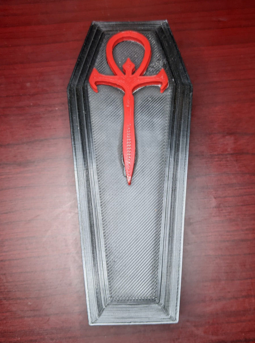 Black 3D printed coffin shaped trinket box with a red symbol on top