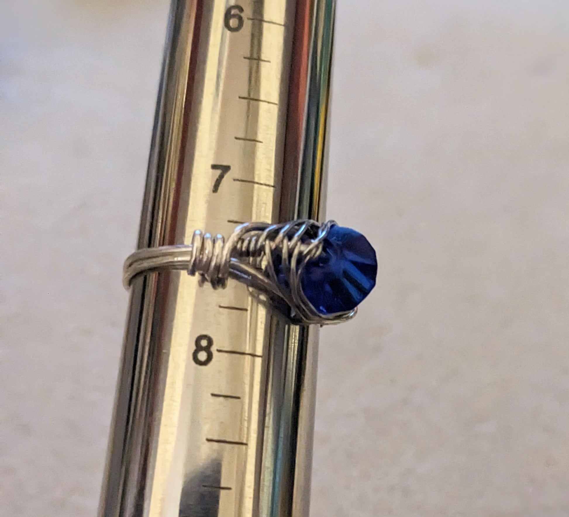 Silver wire wrapped ring with a blue stone on a ring mandrel at size 7.5