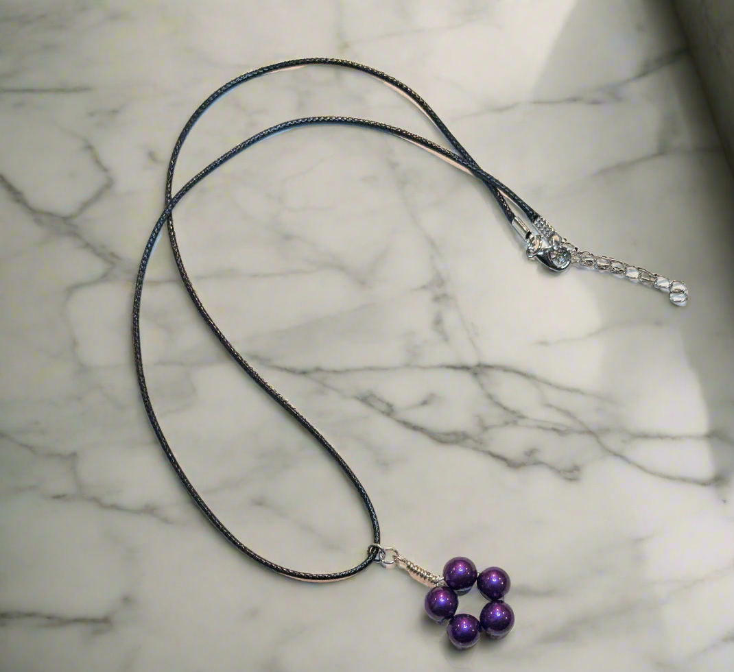 Wire wrapped beaded pendant on a black cord laying on a marbled background. Pendant is crafted from round purple glass pearls