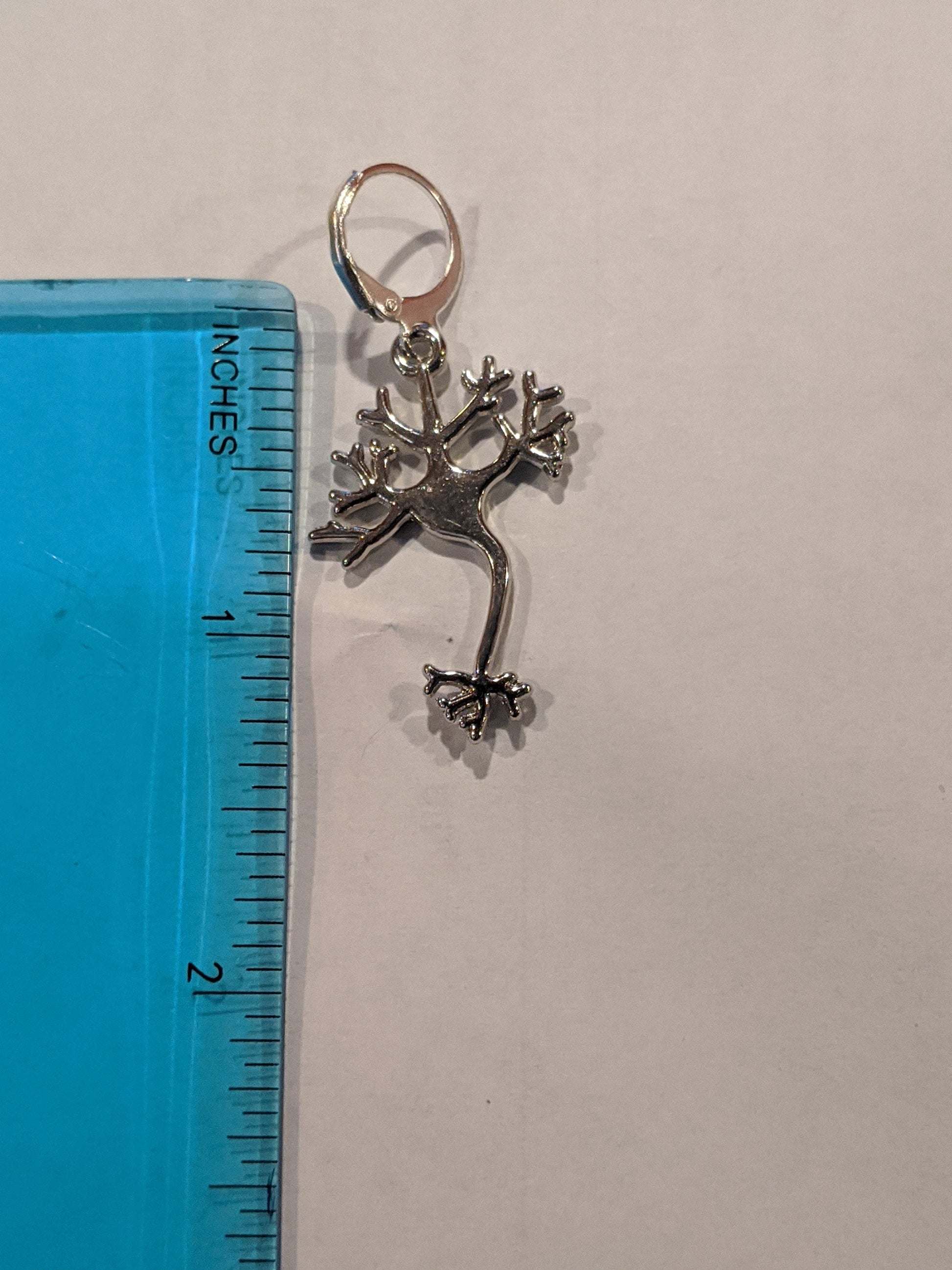 Close up of silver neuron earring next to a blue translucent ruler showing the earring is 1.5 inches long