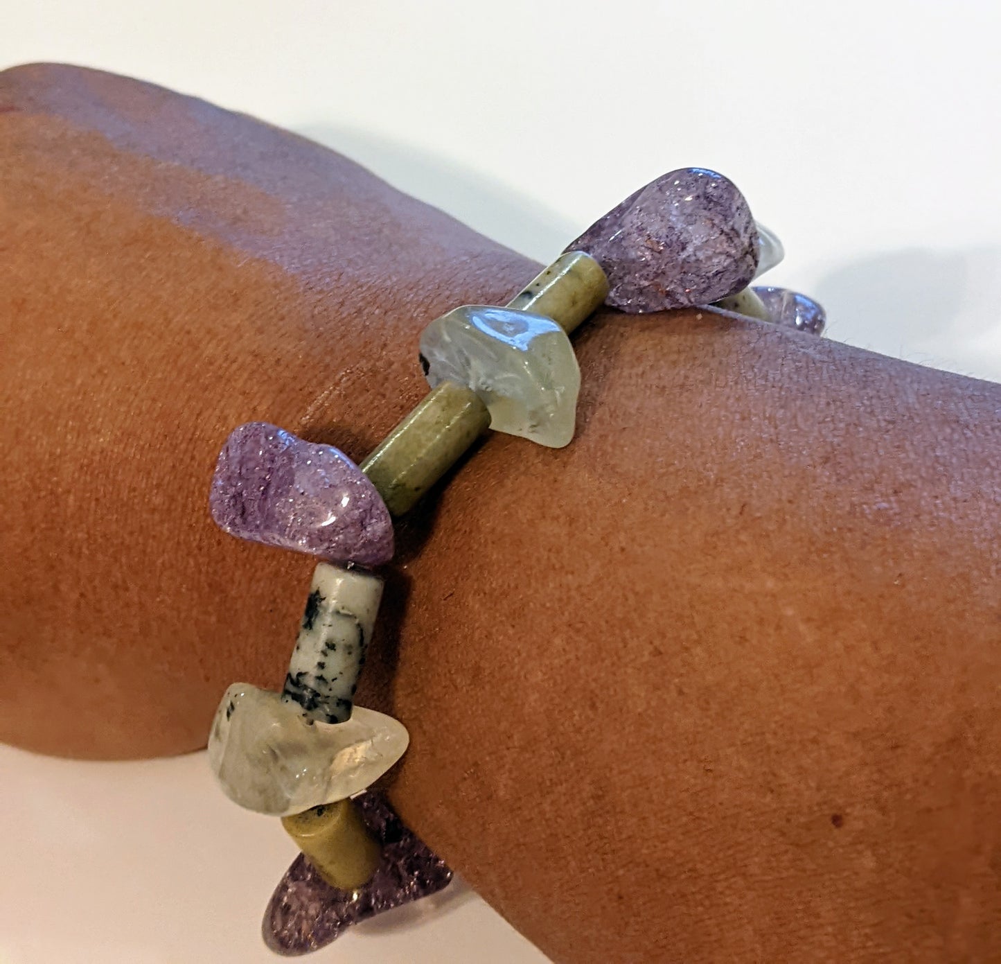 Beaded bracelet on brown person's wrist.  Bracelet is crafted from amethyst and green aventurine nuggets with stone tube beads between. 